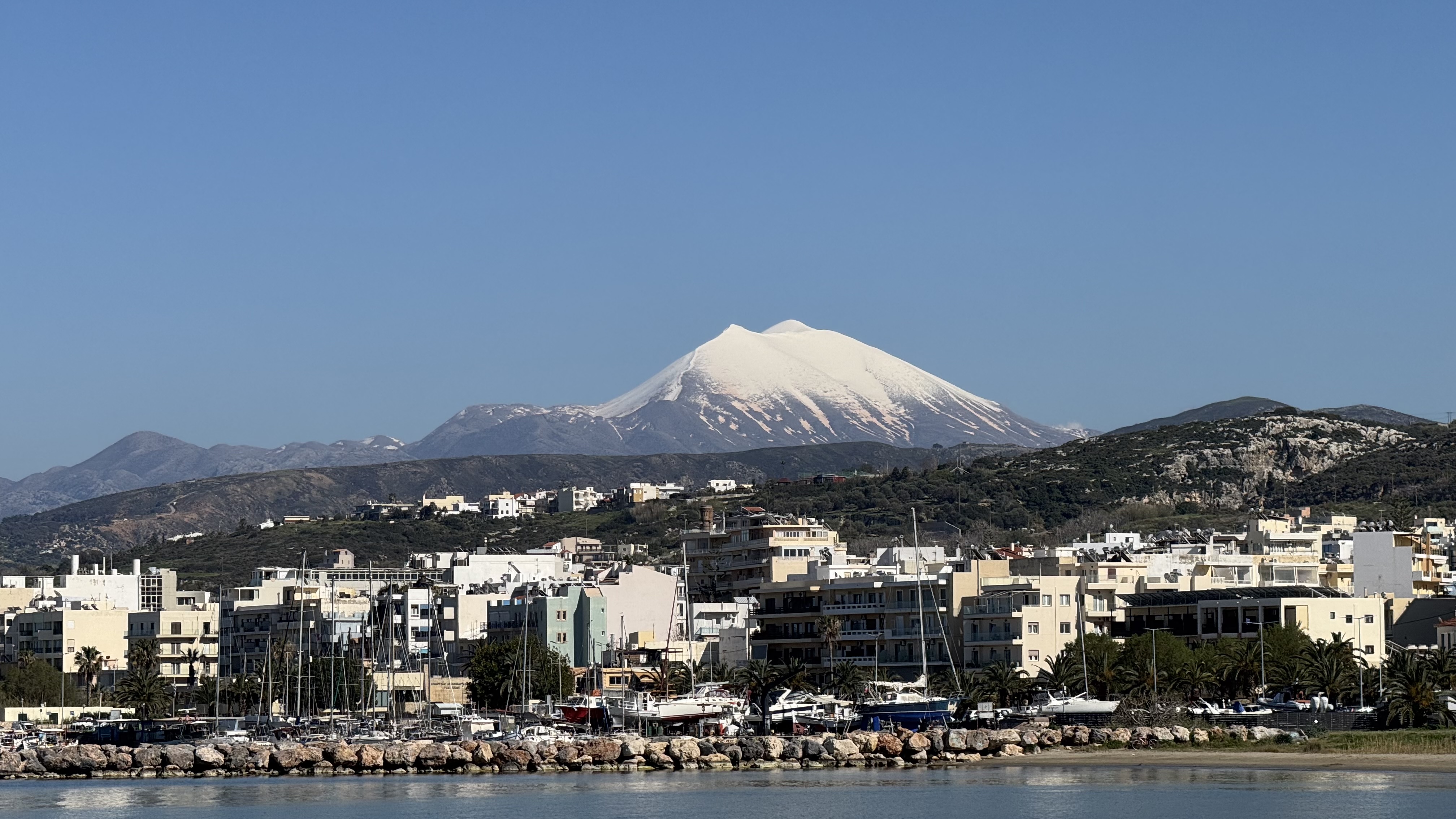 Psiloritis seen from Rethymno old harbor in April — snow-capped peak rising behind the marina and the Venetian-era town